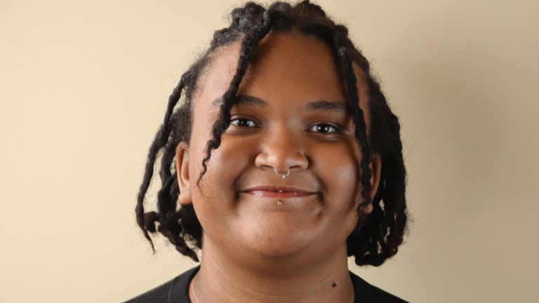 Avaya Hall smiles in front of a beige background. Avaya Hall smiles in front of a beige background.